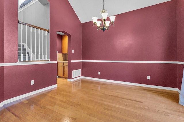 empty room featuring arched walkways, visible vents, light wood-style flooring, a chandelier, and baseboards