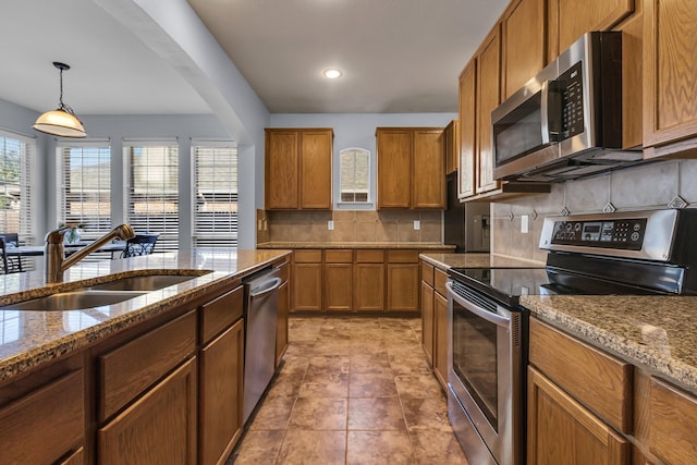 kitchen with stone counters, brown cabinets, stainless steel appliances, tasteful backsplash, and a sink