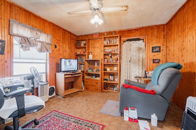 carpeted office space with a ceiling fan, a textured ceiling, and wooden walls