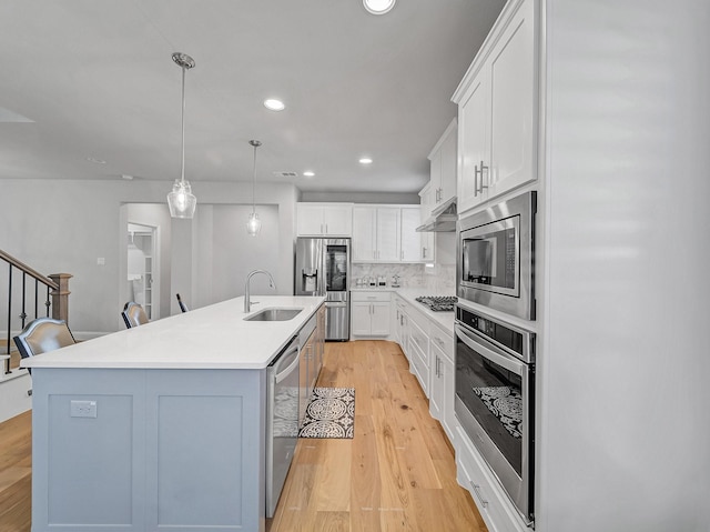 kitchen featuring appliances with stainless steel finishes, light wood-type flooring, under cabinet range hood, white cabinetry, and a sink