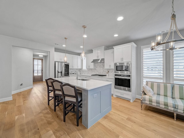 kitchen with stainless steel appliances, decorative backsplash, white cabinetry, a sink, and under cabinet range hood