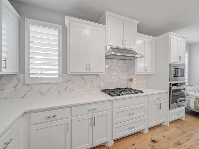 kitchen with light wood-style flooring, decorative backsplash, appliances with stainless steel finishes, white cabinetry, and under cabinet range hood