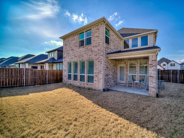 back of house featuring brick siding, a fenced backyard, a lawn, and a patio