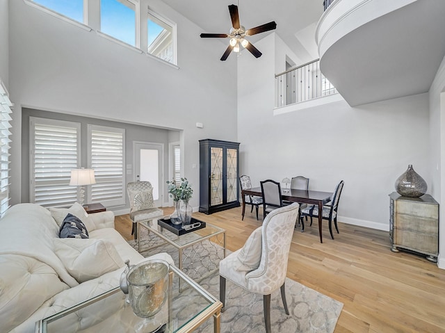 living area featuring a ceiling fan, a high ceiling, baseboards, and wood finished floors