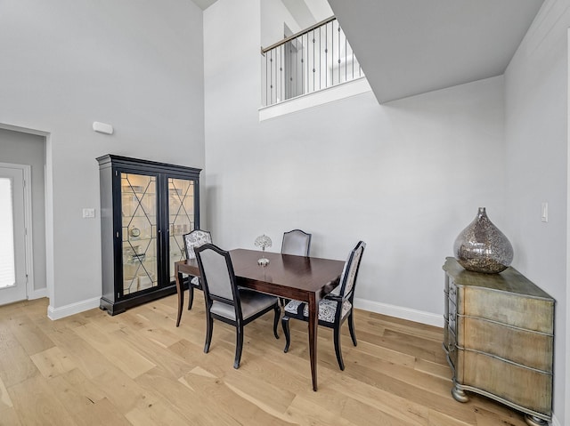 dining room with light wood-style flooring, a high ceiling, and baseboards