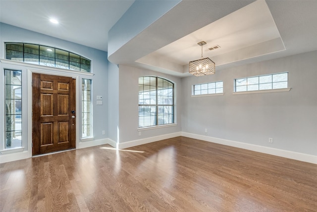 entryway with wood finished floors, a raised ceiling, visible vents, and baseboards