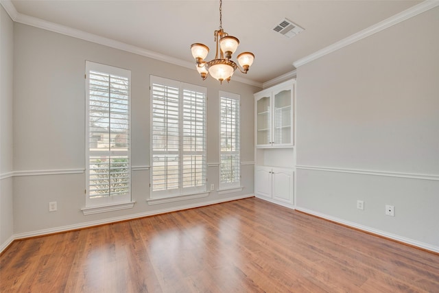 empty room featuring crown molding, visible vents, a chandelier, and wood finished floors