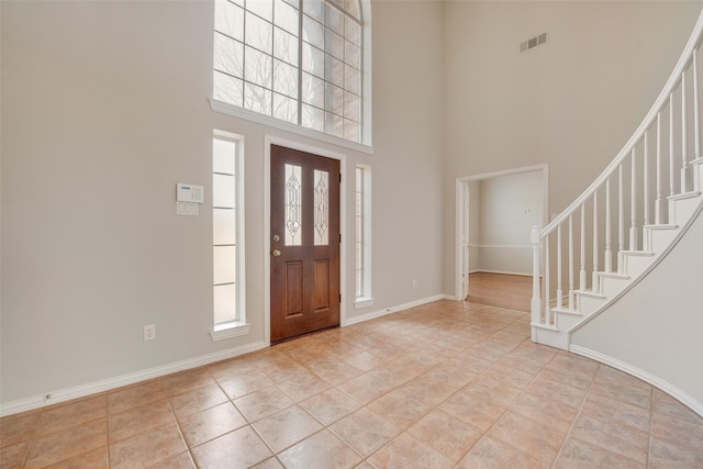 foyer entrance with light tile patterned floors, visible vents, a towering ceiling, stairway, and baseboards