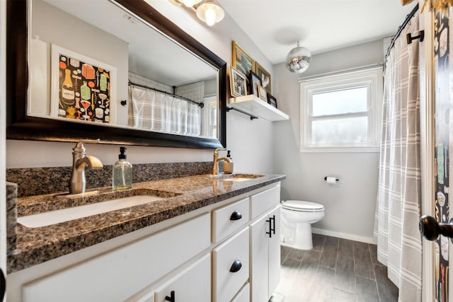 full bath featuring double vanity, a sink, toilet, and baseboards