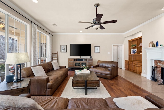 living room with crown molding, a ceiling fan, wood finished floors, a high end fireplace, and visible vents