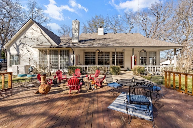 back of house featuring a deck, outdoor dining space, a ceiling fan, a shingled roof, and a chimney