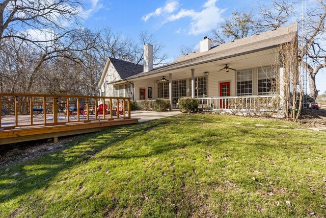 back of property with a ceiling fan, a deck, a yard, and a chimney