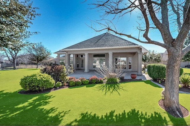 rear view of house featuring roof with shingles, a yard, stucco siding, a patio area, and fence