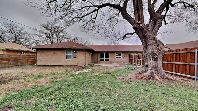 rear view of property featuring a fenced backyard, brick siding, a patio, and a lawn