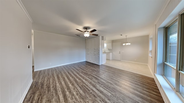 unfurnished living room with dark wood-style floors, ceiling fan with notable chandelier, baseboards, and crown molding