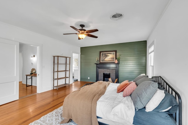 bedroom featuring a fireplace, visible vents, ceiling fan, wood finished floors, and baseboards