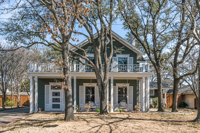 view of front facade with a balcony, covered porch, and fence