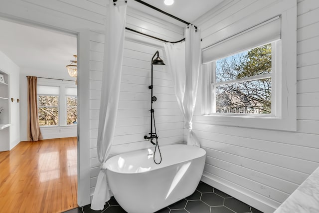 bathroom featuring a soaking tub, a healthy amount of sunlight, and wooden walls