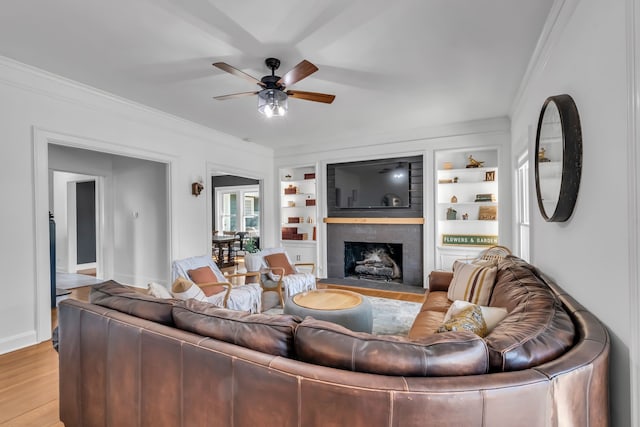 living area featuring light wood-style floors, a fireplace with flush hearth, built in features, and crown molding