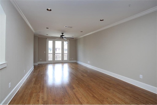 empty room with baseboards, visible vents, ceiling fan, wood finished floors, and crown molding