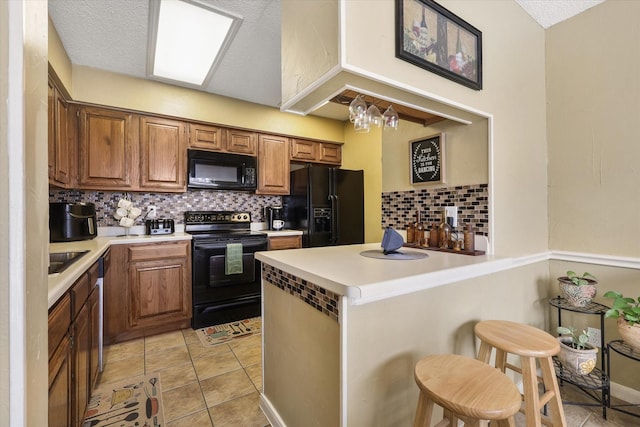 kitchen with light tile patterned floors, a peninsula, light countertops, black appliances, and a kitchen bar