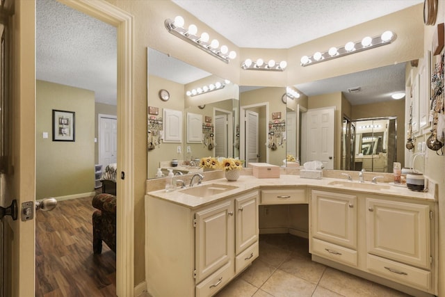 bathroom with a sink, a textured ceiling, ensuite bathroom, and double vanity