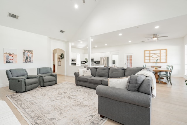 living room with light wood-style floors, ceiling fan, visible vents, and arched walkways