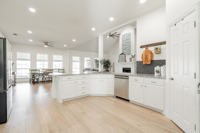 kitchen with a peninsula, stainless steel appliances, white cabinets, light stone countertops, and light wood finished floors