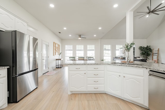 kitchen with light stone counters, light wood finished floors, appliances with stainless steel finishes, a ceiling fan, and a sink