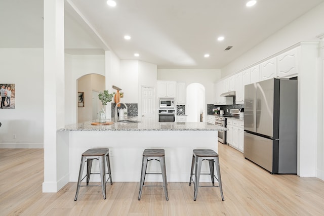 kitchen with appliances with stainless steel finishes, a sink, a peninsula, light stone countertops, and under cabinet range hood