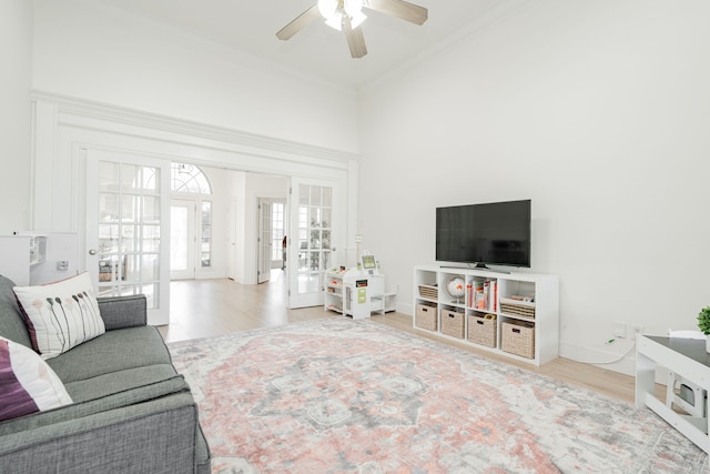 living area featuring wood finished floors, a ceiling fan, baseboards, ornamental molding, and french doors