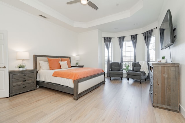 bedroom with ornamental molding, a tray ceiling, visible vents, and light wood-style floors