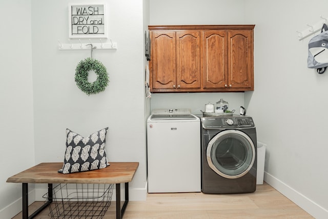 laundry area featuring cabinet space, baseboards, light wood finished floors, and washing machine and clothes dryer