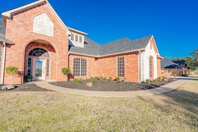 view of front of house featuring brick siding, a front lawn, and roof with shingles