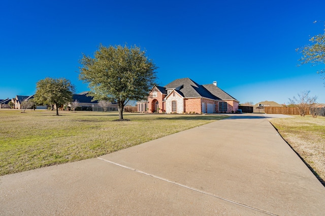 view of front of home with brick siding, fence, concrete driveway, a front lawn, and a chimney