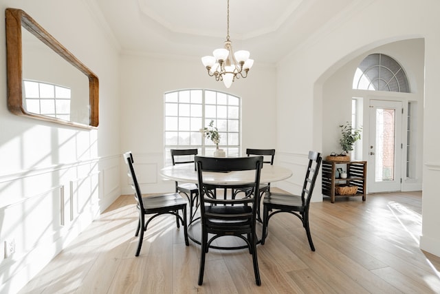 dining area with a decorative wall, light wood-type flooring, a raised ceiling, and a notable chandelier