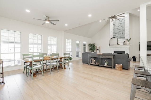 dining space with ceiling fan, light wood-style floors, a fireplace, high vaulted ceiling, and recessed lighting