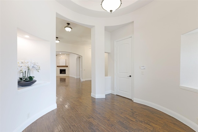 corridor featuring arched walkways, dark wood finished floors, and baseboards