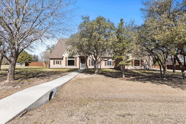 view of property hidden behind natural elements with fence and brick siding