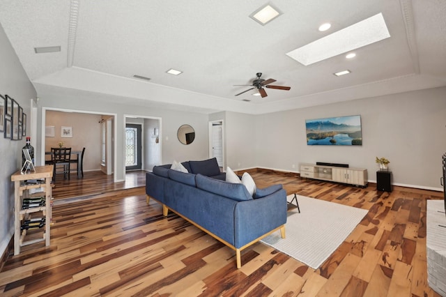 living room with a tray ceiling, a skylight, wood finished floors, and baseboards