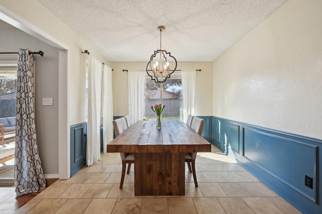 dining area with light tile patterned floors, a textured ceiling, a decorative wall, a wainscoted wall, and a notable chandelier