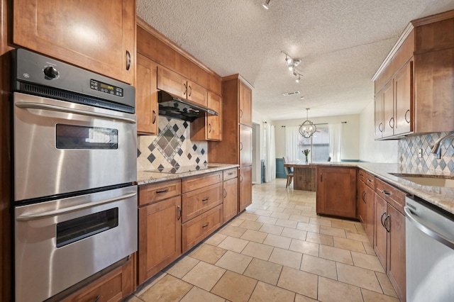 kitchen with stainless steel appliances, brown cabinetry, a sink, a peninsula, and under cabinet range hood