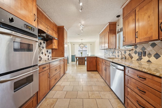 kitchen featuring a peninsula, a sink, appliances with stainless steel finishes, decorative backsplash, and brown cabinetry