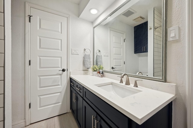 bathroom featuring a textured wall, wood finished floors, vanity, and visible vents