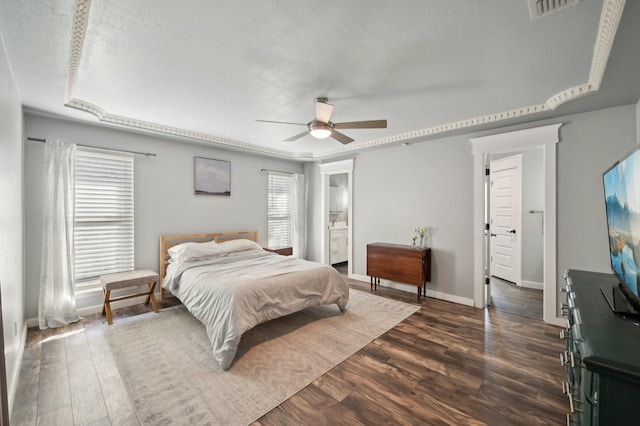 bedroom featuring dark wood finished floors, visible vents, ceiling fan, ensuite bath, and baseboards