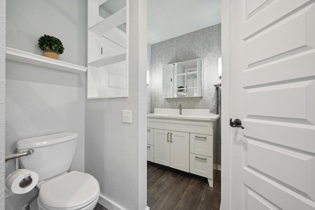 half bathroom featuring baseboards, a textured wall, toilet, wood finished floors, and vanity