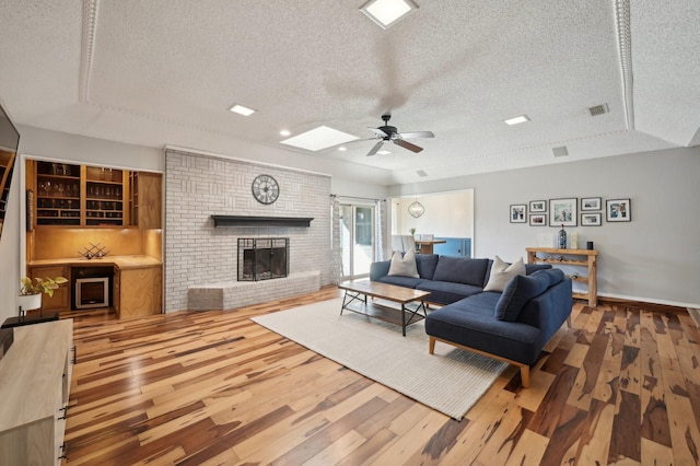 living room with a brick fireplace, wood finished floors, visible vents, and a ceiling fan