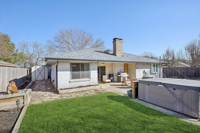 rear view of property with brick siding, a lawn, a hot tub, a patio area, and a fenced backyard