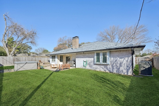 rear view of house with a fenced backyard, cooling unit, brick siding, a lawn, and a chimney