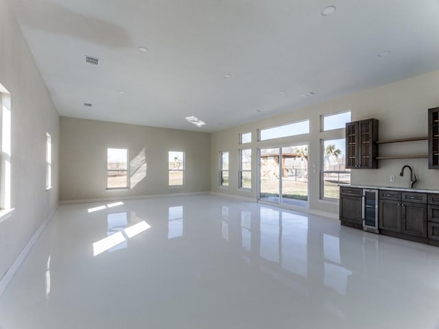 unfurnished living room with plenty of natural light, wine cooler, baseboards, and a sink